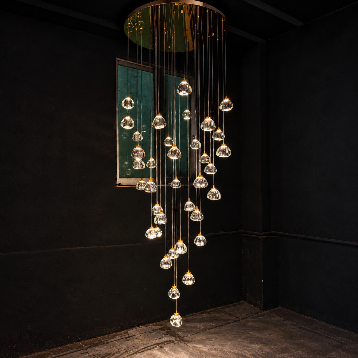 A modern multi-light chandelier with clear glass teardrop pendant bulbs suspended from a circular gold-toned metal frame, hanging in a cascading waterfall pattern against a dark black wall.