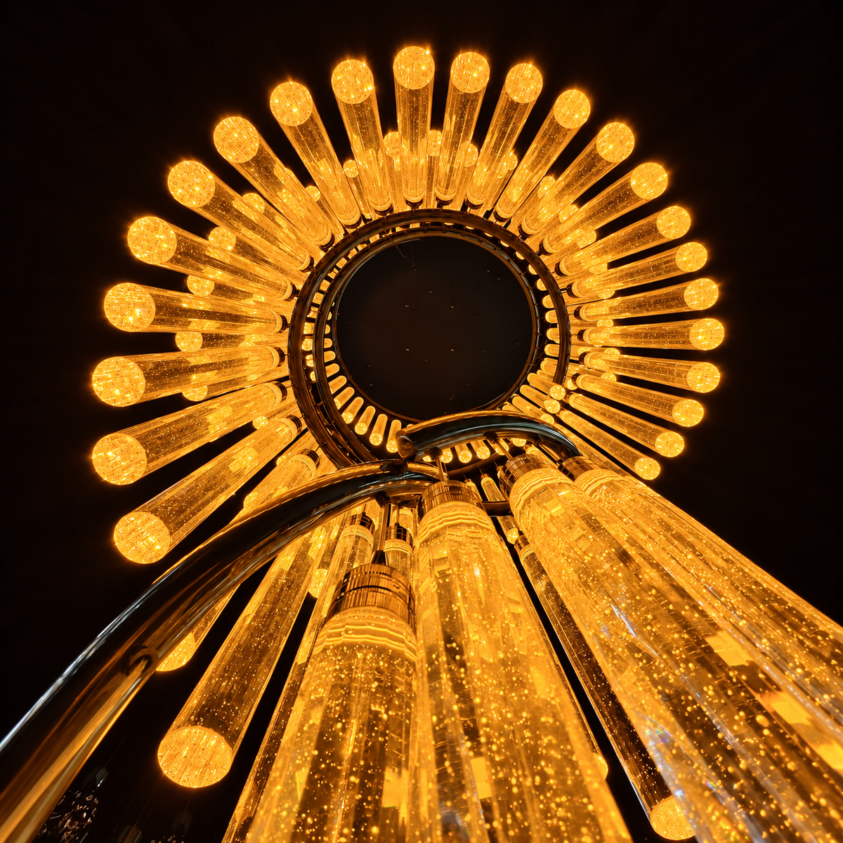 Low-angle view of a spiral chandelier with glowing amber crystal rods and curved metal supports against a dark background.