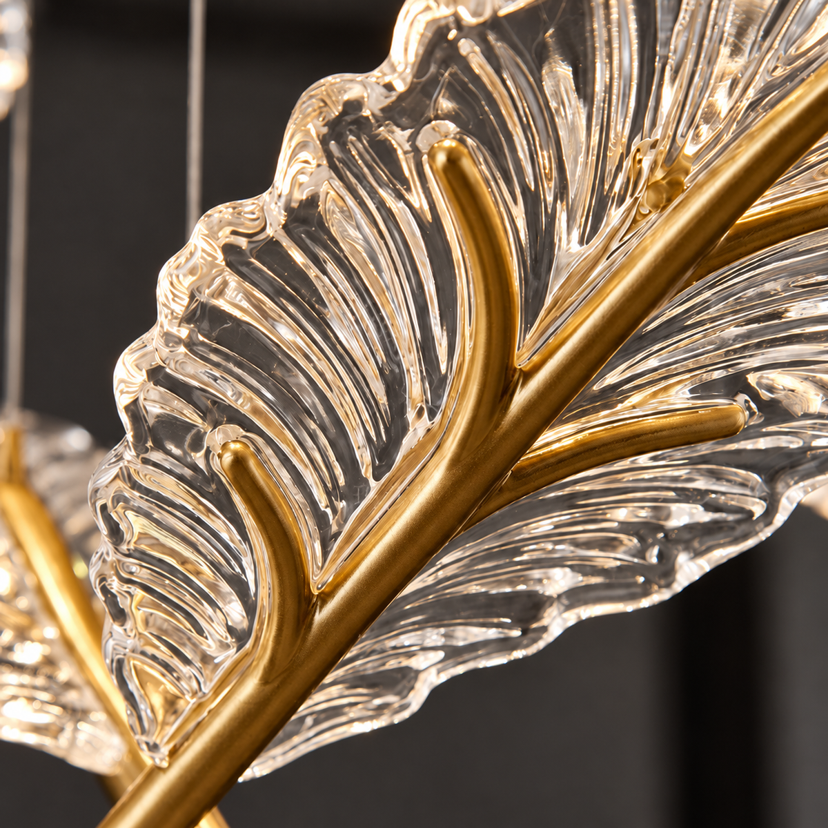 Close-up of the chandelier’s clear, ridged acrylic feather pendant with a gold-tone central stem against a dark background.