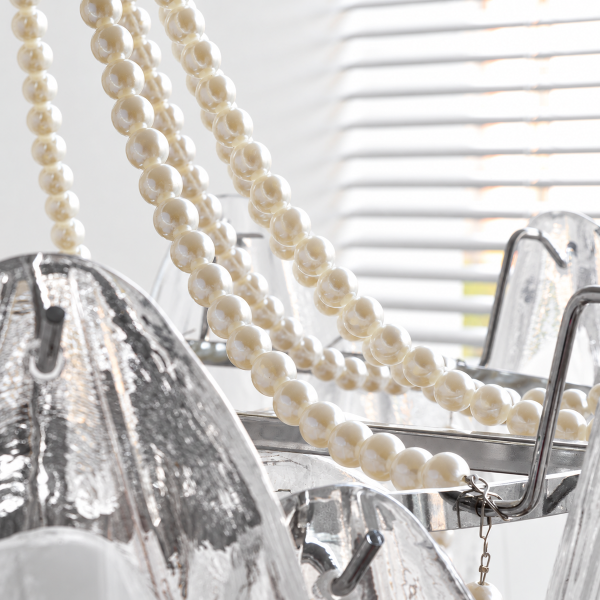 A close-up of a modern chandelier featuring a prominent strand of cream pearl beads draped over clear glass and textured silver metal arms.