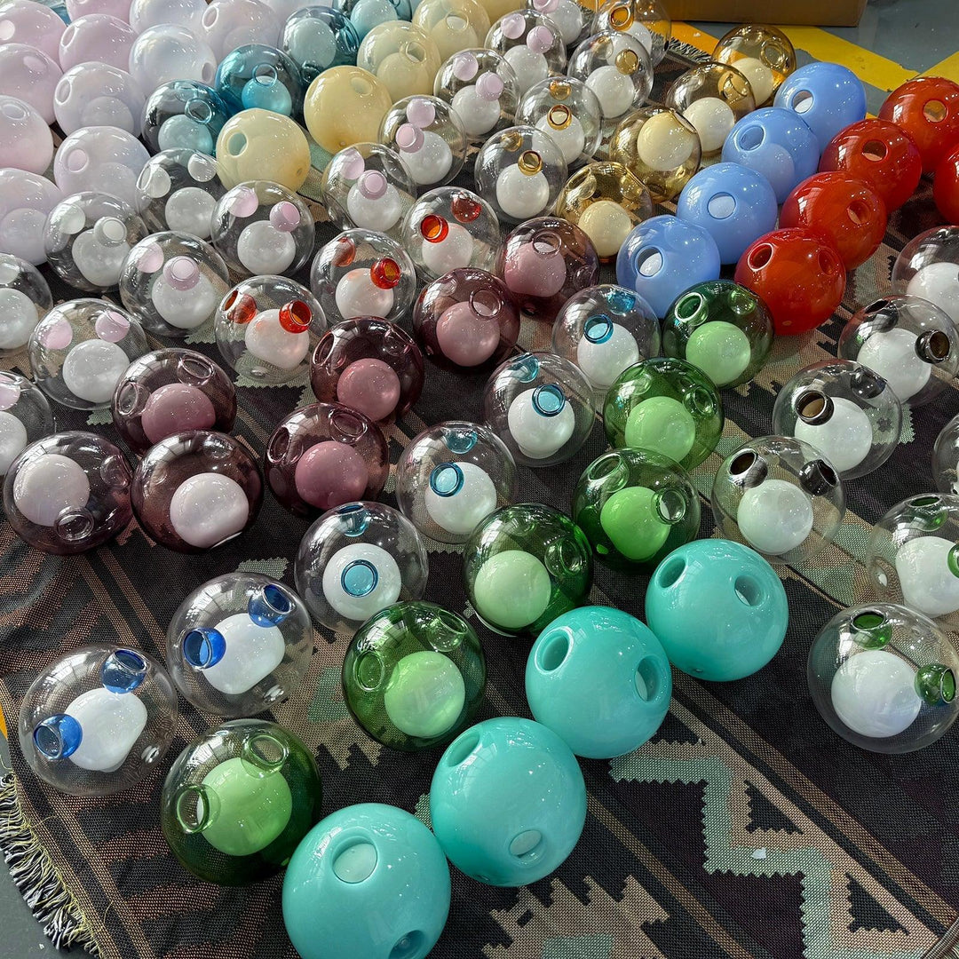 Chandelier glass globes in clear, turquoise, green, red, blue and pastel colors are arranged in rows on a patterned rug.