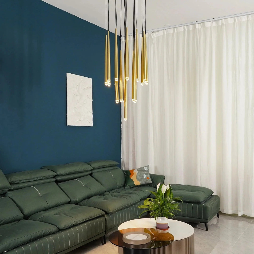 A modern living room featuring a dark green sectional sofa, a dark blue accent wall with a white abstract painting, and a multi-light pendant chandelier with gold and black rods.