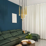 A modern living room featuring a dark green sectional sofa, a dark blue accent wall with a white abstract painting, and a multi-light pendant chandelier with gold and black rods.