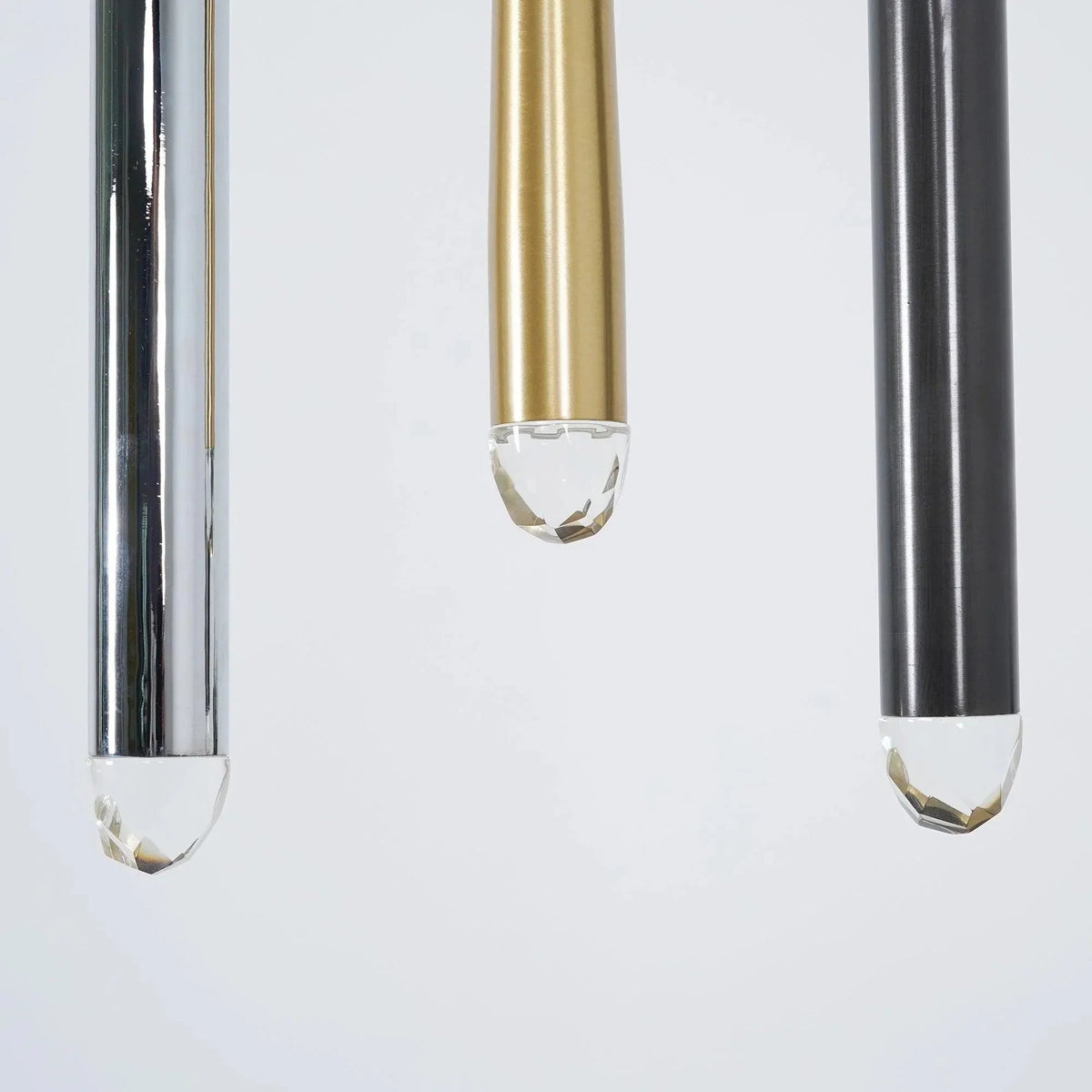 Chandelier detail showing silver, brass, and black tubes with clear faceted crystal tips against a pale background.