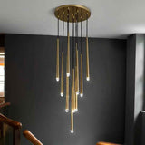 A modern chandelier with a circular gold ceiling mount, multiple vertical gold rods, black hanging cords, and small glowing bulbs, shown installed in a real interior with a dark gray wall and staircase railings.