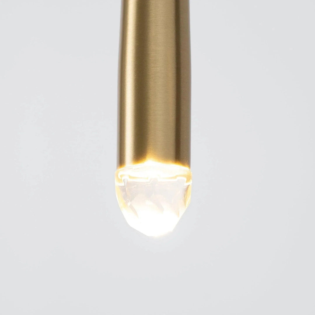 Close-up of a chandelier brass tube with an illuminated crystal tip against a pale gray background.
