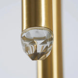 Close-up of an unlit clear faceted crystal tip on a brass chandelier tube against a pale gray background.