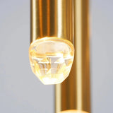 Close-up of an illuminated faceted crystal tip on a brass chandelier tube, with another brass tube behind it.