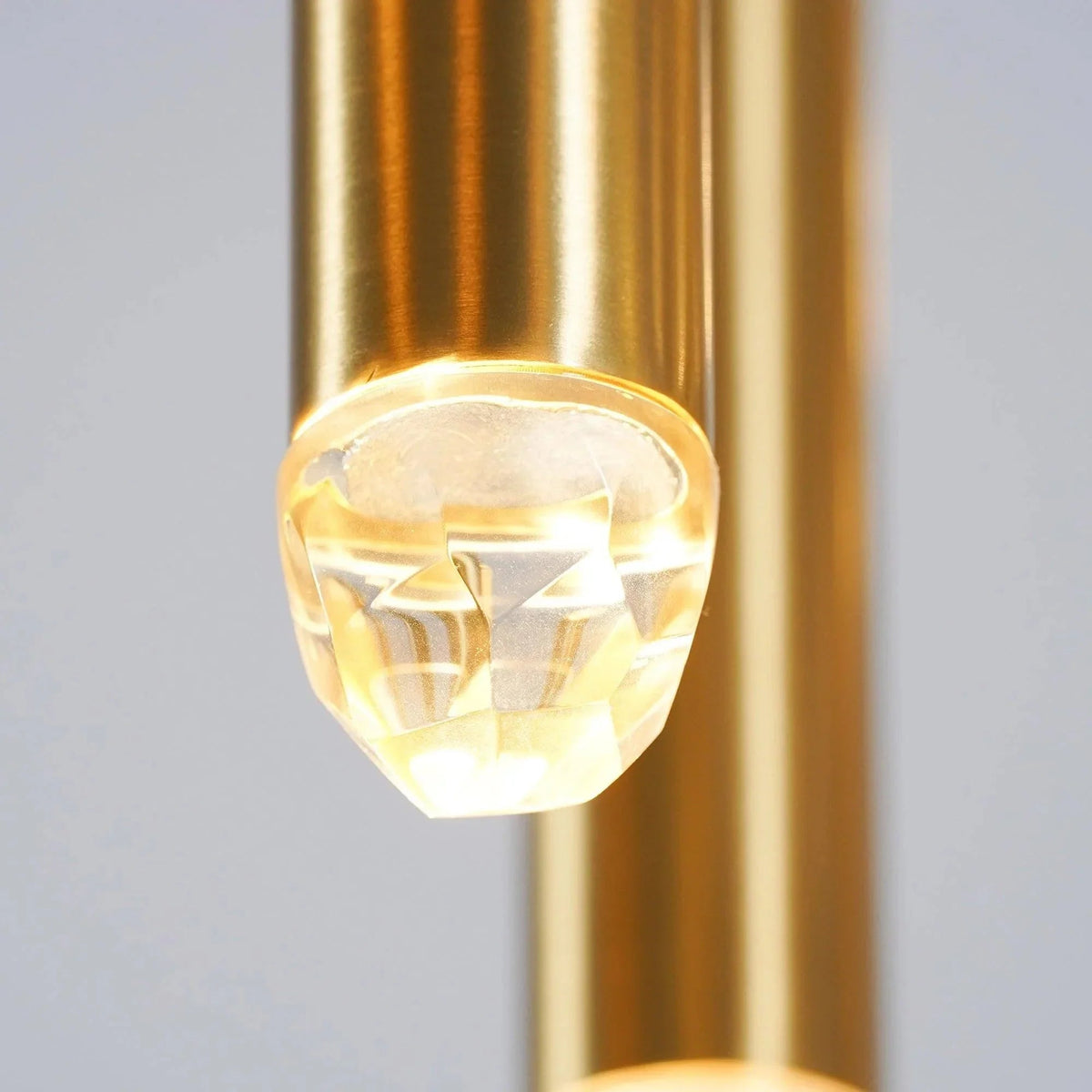 Close-up of an illuminated faceted crystal tip on a brass chandelier tube, with another brass tube behind it.