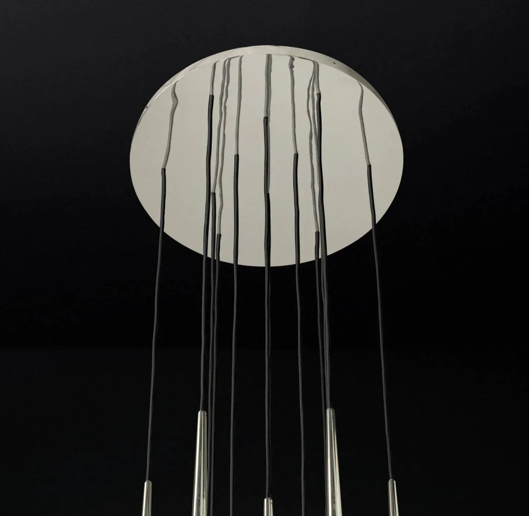 Chandelier canopy detail with a reflective silver circular ceiling plate and black suspension cords against a dark background.
