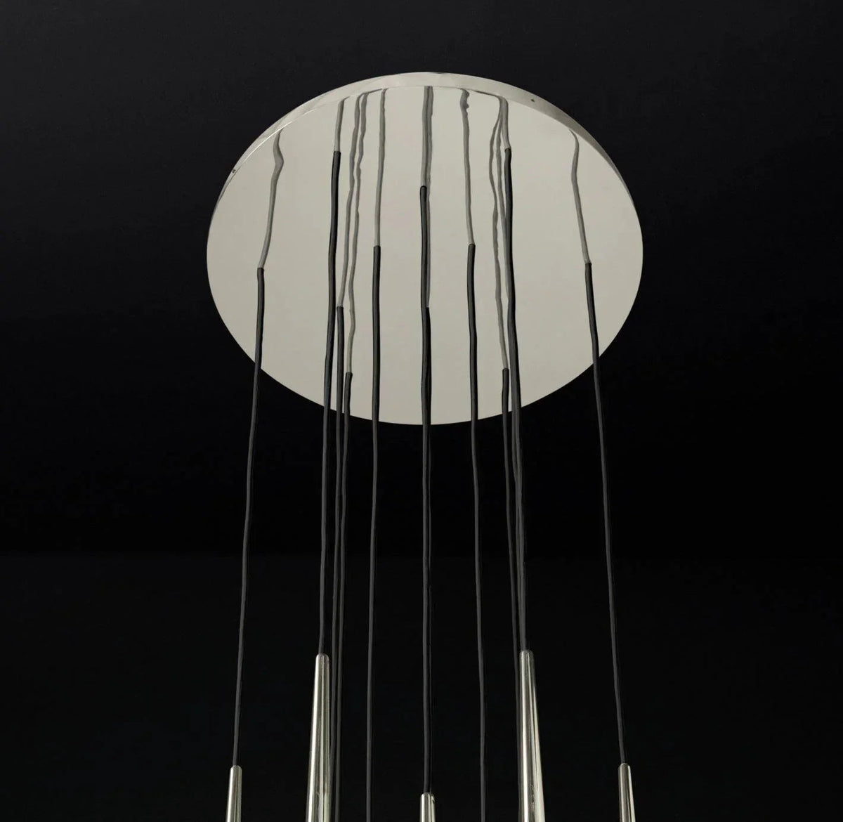 Chandelier canopy detail with a reflective silver circular ceiling plate and black suspension cords against a dark background.