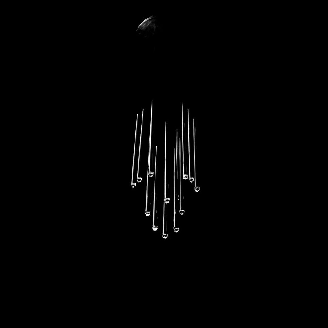A modern chandelier with multiple clear glass or acrylic rods hanging from a dark ceiling mount against a solid black background.