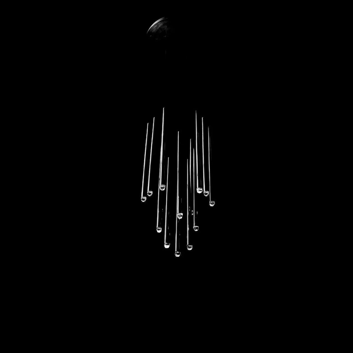 A modern chandelier with multiple clear glass or acrylic rods hanging from a dark ceiling mount against a solid black background.