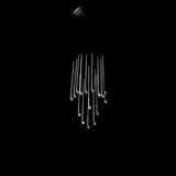 A modern chandelier with multiple clear glass rods of varying lengths hanging from a dark ceiling mount against a solid black background.