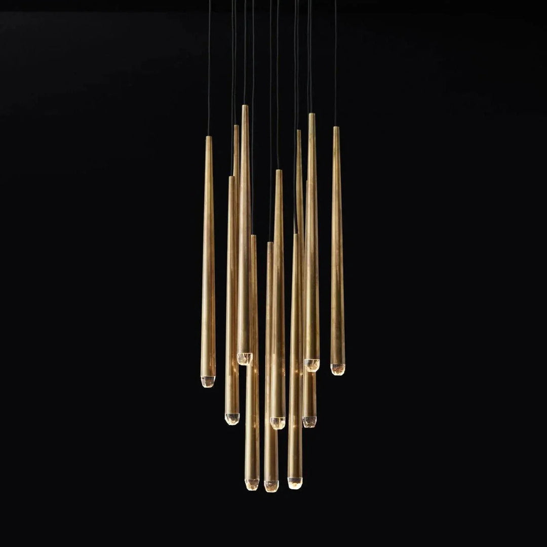A modern multi-light linear chandelier with brushed gold metal tubes suspended by thin black cords against a solid black background.