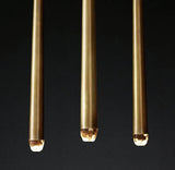Close-up of three brass chandelier tubes with illuminated crystal tips against a dark background.