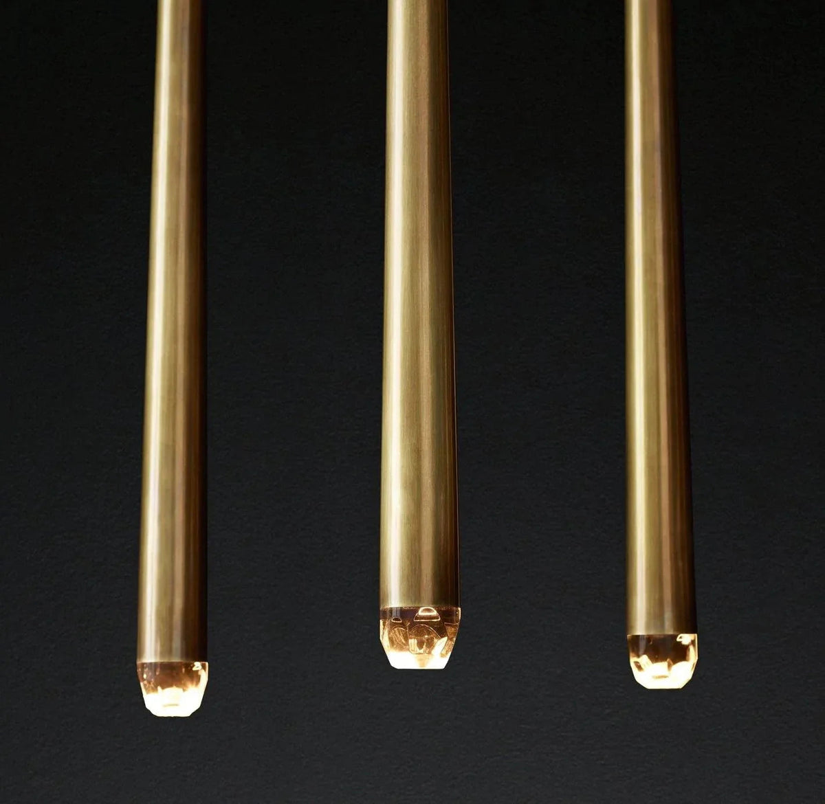 Close-up of three brass chandelier tubes with illuminated crystal tips against a dark background.