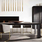 Slim brass tube chandelier drops in a row above a dark wood dining table beside a black fireplace and cabinet.