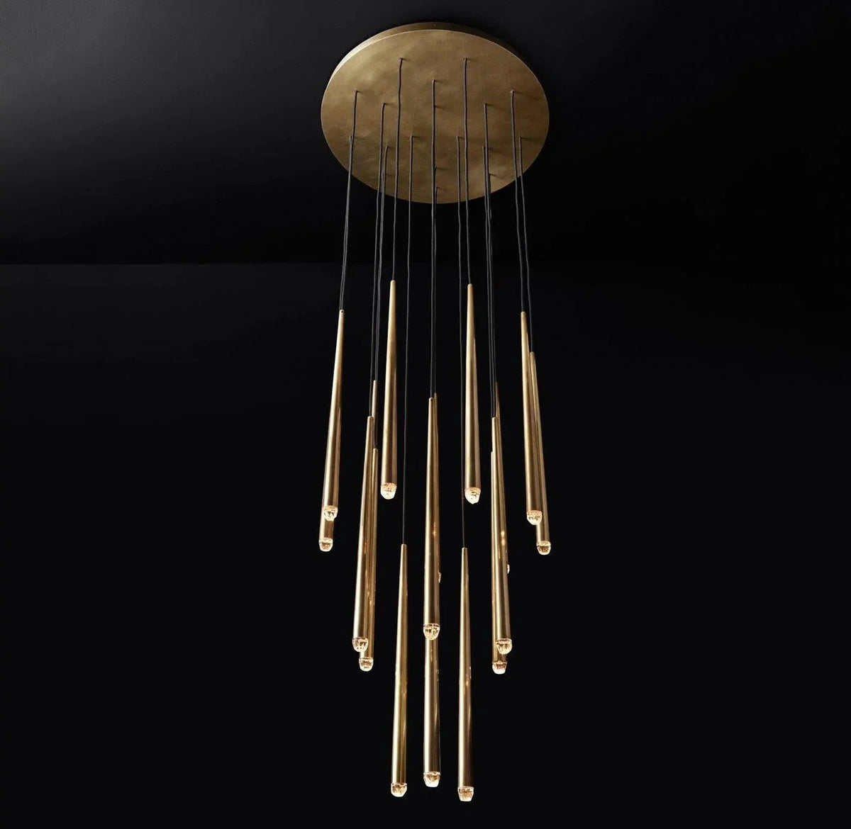 A modern chandelier with a circular brushed brass ceiling canopy and multiple vertical glass tubes in varying lengths, shown against a solid black background.