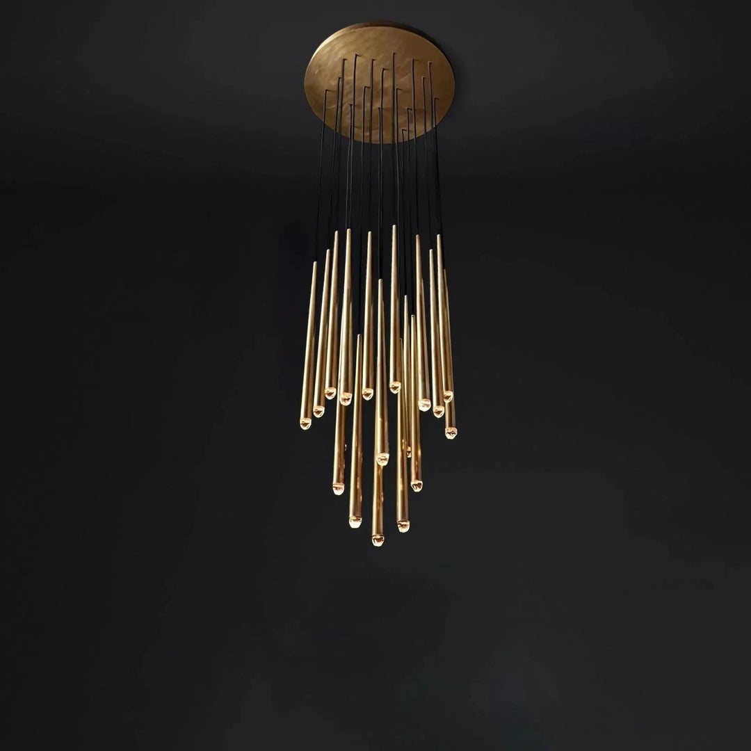 A modern chandelier with a circular gold ceiling mount and multiple hanging gold glass rods suspended by black cords, shown against a dark black background.