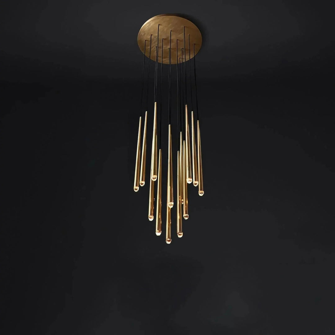 A modern chandelier with a circular brushed gold ceiling mount and multiple hanging cylindrical glass tubes, shown against a dark black background.