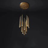 A modern chandelier with a circular brushed gold ceiling mount and multiple hanging cylindrical glass tubes, shown against a dark black background.