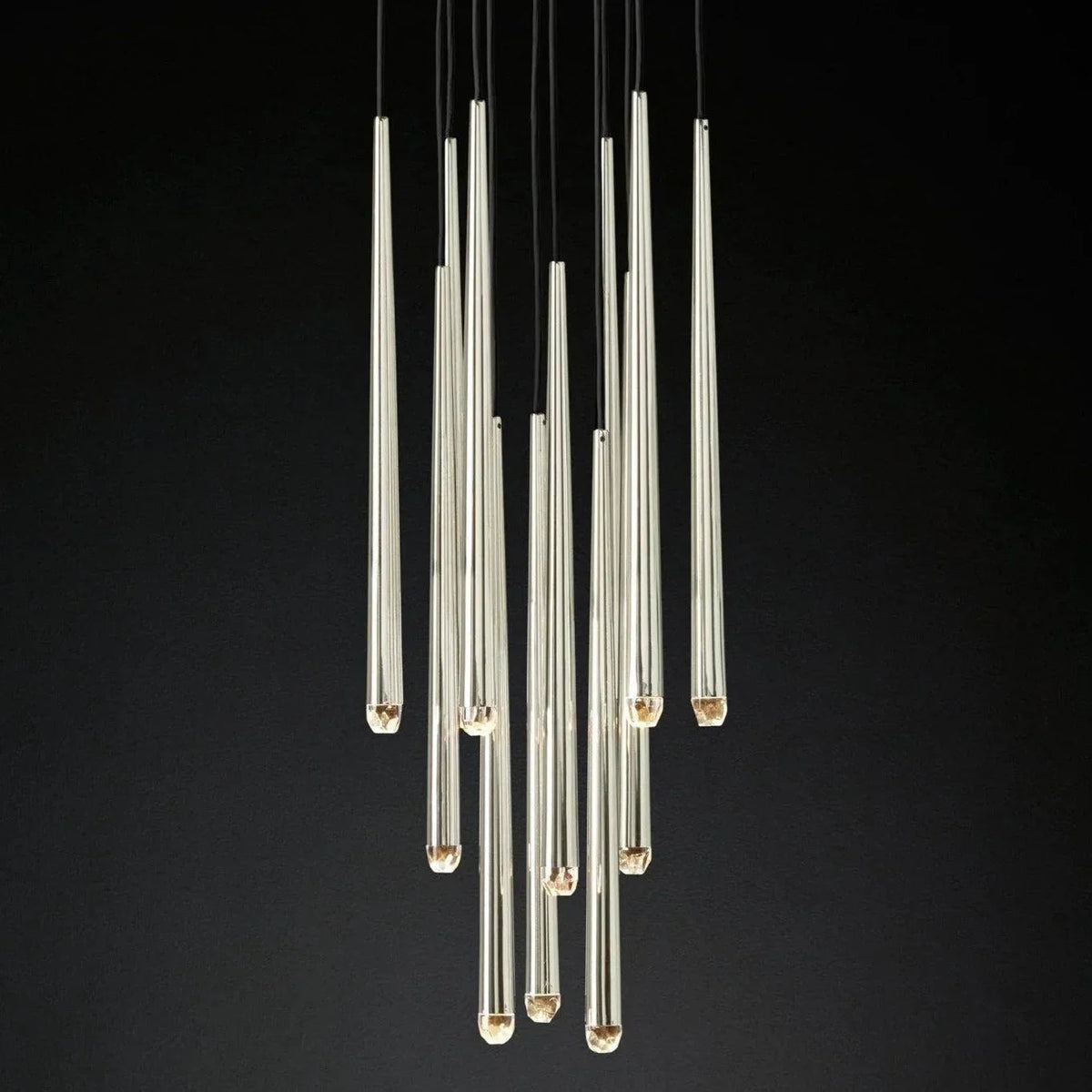 A modern multi-light chandelier featuring multiple clear glass cylindrical tubes of varying lengths suspended from black cords against a solid black background.