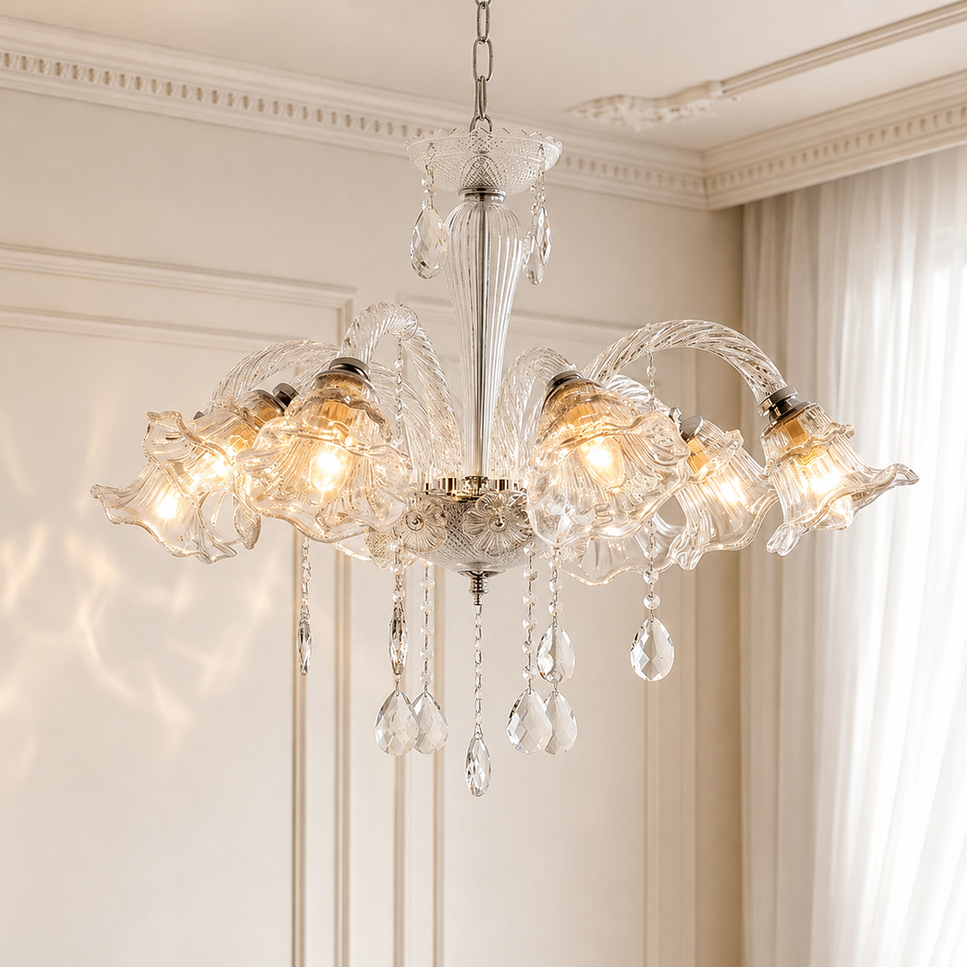 A multi-light crystal chandelier with ornate glass shades and hanging teardrop pendants, shown illuminated in a classic cream-colored room with decorative wall molding and curtains.