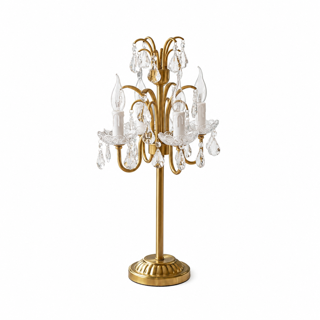 Antique brass table lamp with curved arms, candle-style lights, clear crystal drops, and a round base against a white background.