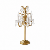 Antique brass table lamp with curved arms, candle-style lights, clear crystal drops, and a round base against a white background.