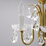 Close-up of the antique brass table lamp showing a candle-style light, clear crystal dish, and hanging crystal drops against a gray background.