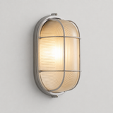 A modern industrial wall sconce with a ribbed clear glass shade, a silver metal cage guard, and a brushed silver metal frame, shown illuminated against a neutral light gray wall.