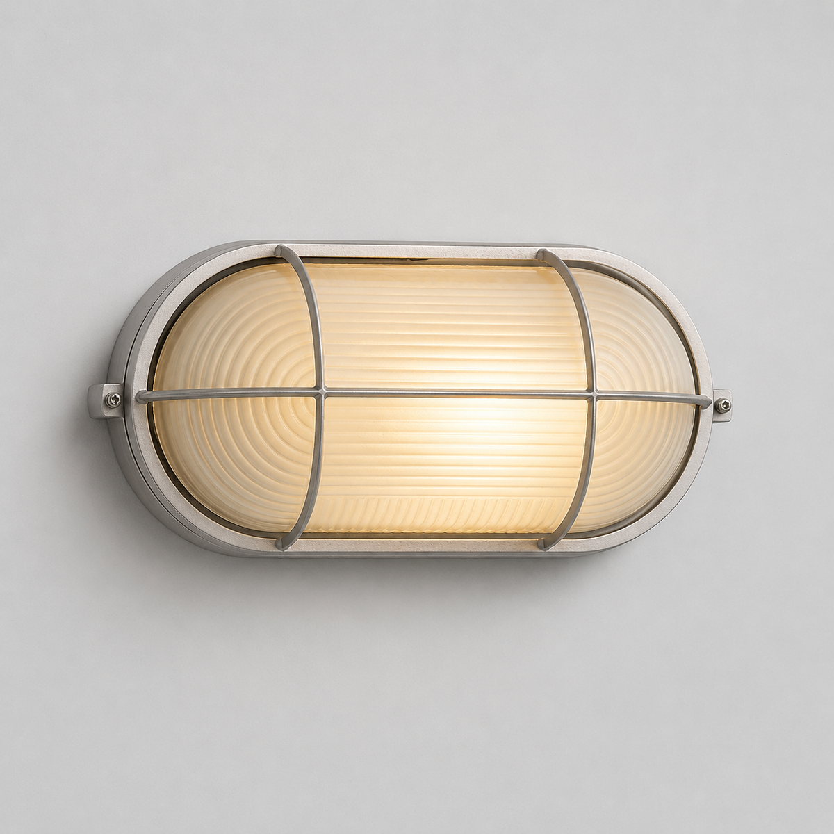 A silver wall sconce with ribbed frosted glass glows warmly, mounted horizontally on a light gray wall.