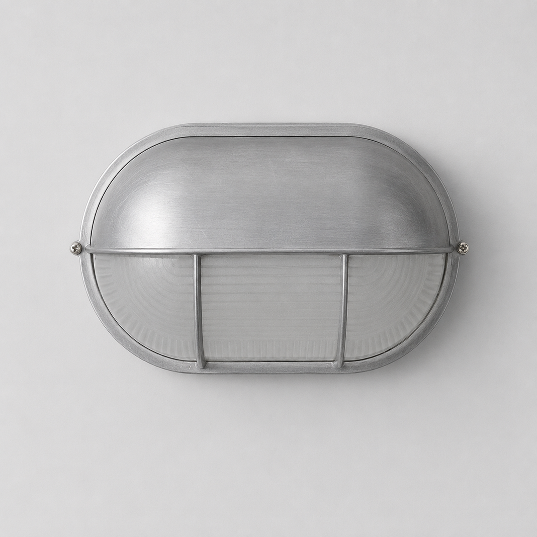 Oval wall sconce with a brushed silver metal hood and ribbed glass diffuser against a light gray background.