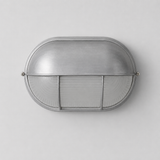 Oval wall sconce with a brushed silver metal hood and ribbed glass diffuser against a light gray background.
