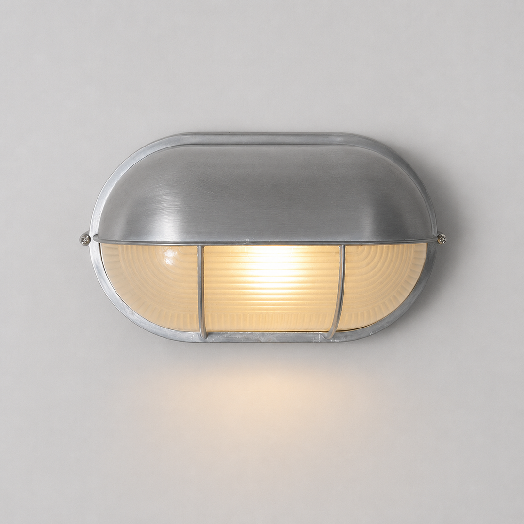 A modern oval wall sconce with a brushed silver metal frame and a warm yellow illuminated glass shade, shown against a neutral light gray background.