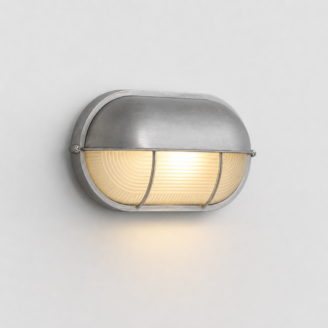 A modern dome-shaped wall sconce with a brushed silver metal finish and a warm yellow glowing light inside a ribbed glass shade, mounted on a plain light gray wall.