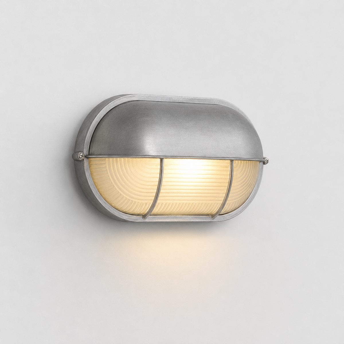 A modern dome-shaped wall sconce with a brushed silver metal finish and a warm yellow glowing light inside a ribbed glass shade, mounted on a plain light gray wall.