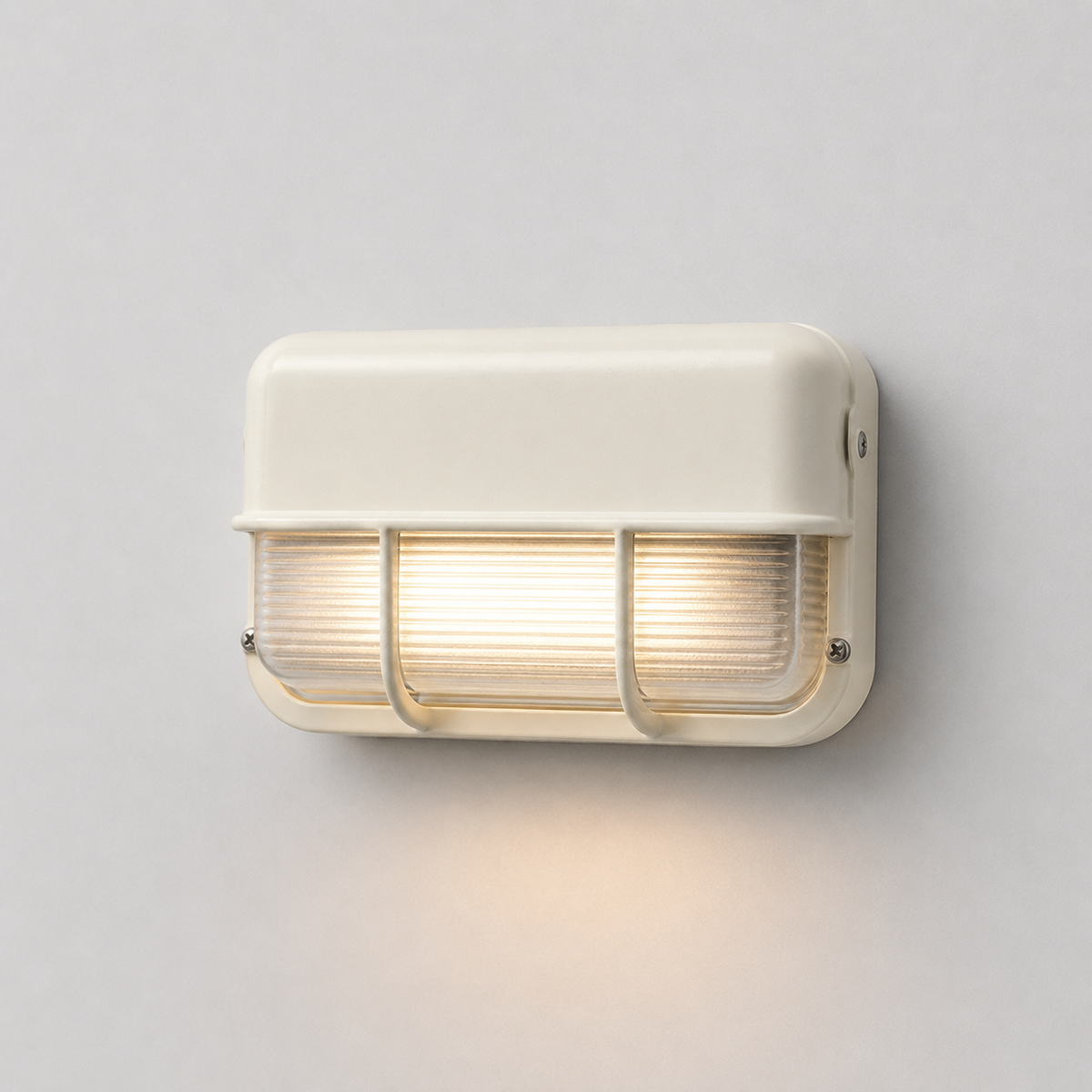 Off-white wall sconce with ribbed glass and protective bars, viewed at an angle and casting warm light down a pale gray wall.