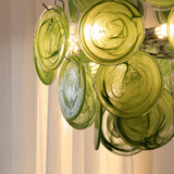 A close-up of a modern chandelier featuring multiple circular green glass discs with swirling patterns, illuminated by warm light from visible bulbs.