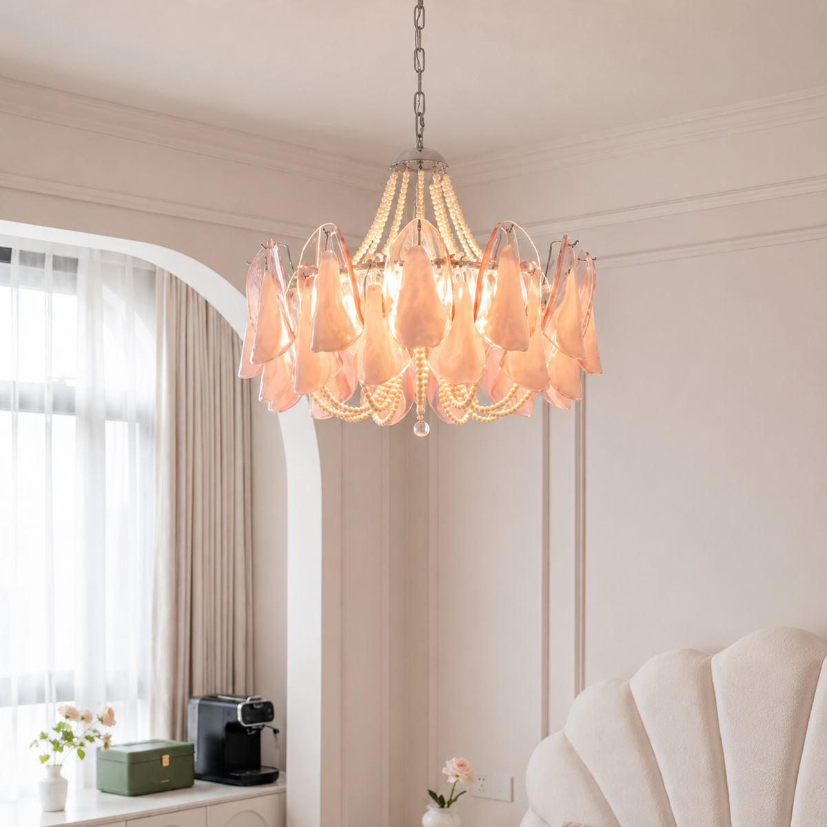 A modern chandelier with soft pink glass petal-like shades and clear crystal accents, hanging in a bright, elegant room with cream walls and an arched window.