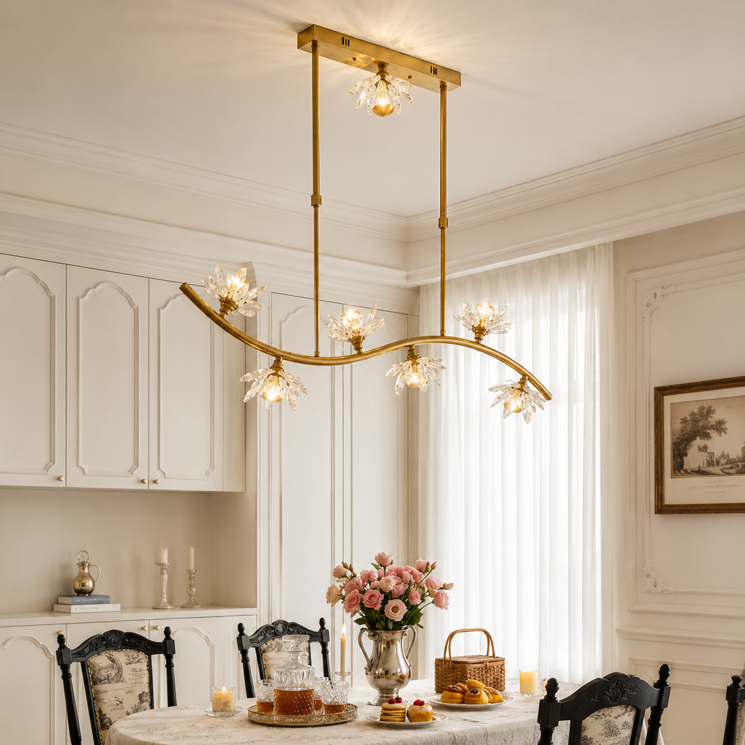 A modern brass six-light linear chandelier with clear glass crystal flower shades hanging over a dining table in a beautifully decorated dining room.
