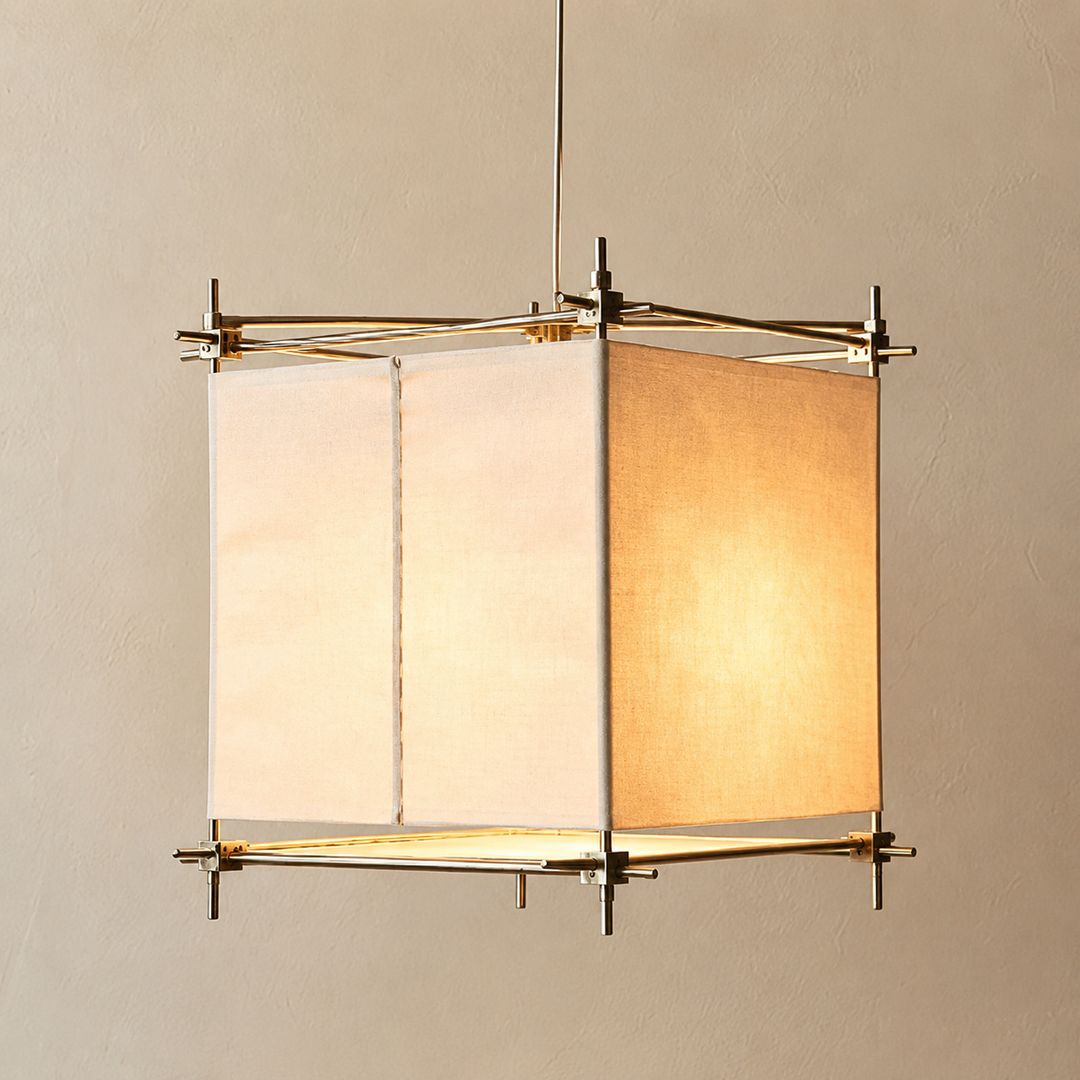 A hanging lamp with cream fabric panels and a gold-toned frame glows warmly against a beige wall.