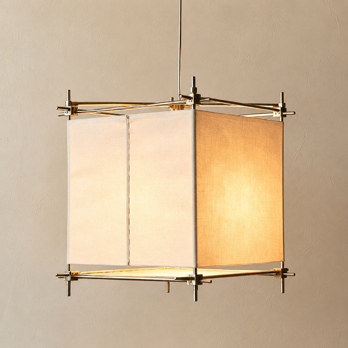A hanging lamp with cream fabric panels and a gold-toned frame glows warmly against a beige wall.