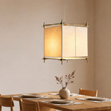 A cream fabric hanging lamp with a gold-toned frame hangs above a wooden dining table set with plates and a vase.