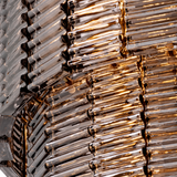 Close-up of a textured glass chandelier or light fixture with multiple curved glass tubes arranged in vertical rows, showing warm golden light reflecting off a smoky amber-tinted glass.