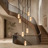 A marble chandelier with glowing cream shades hangs from long black chains through the center of a curved staircase.