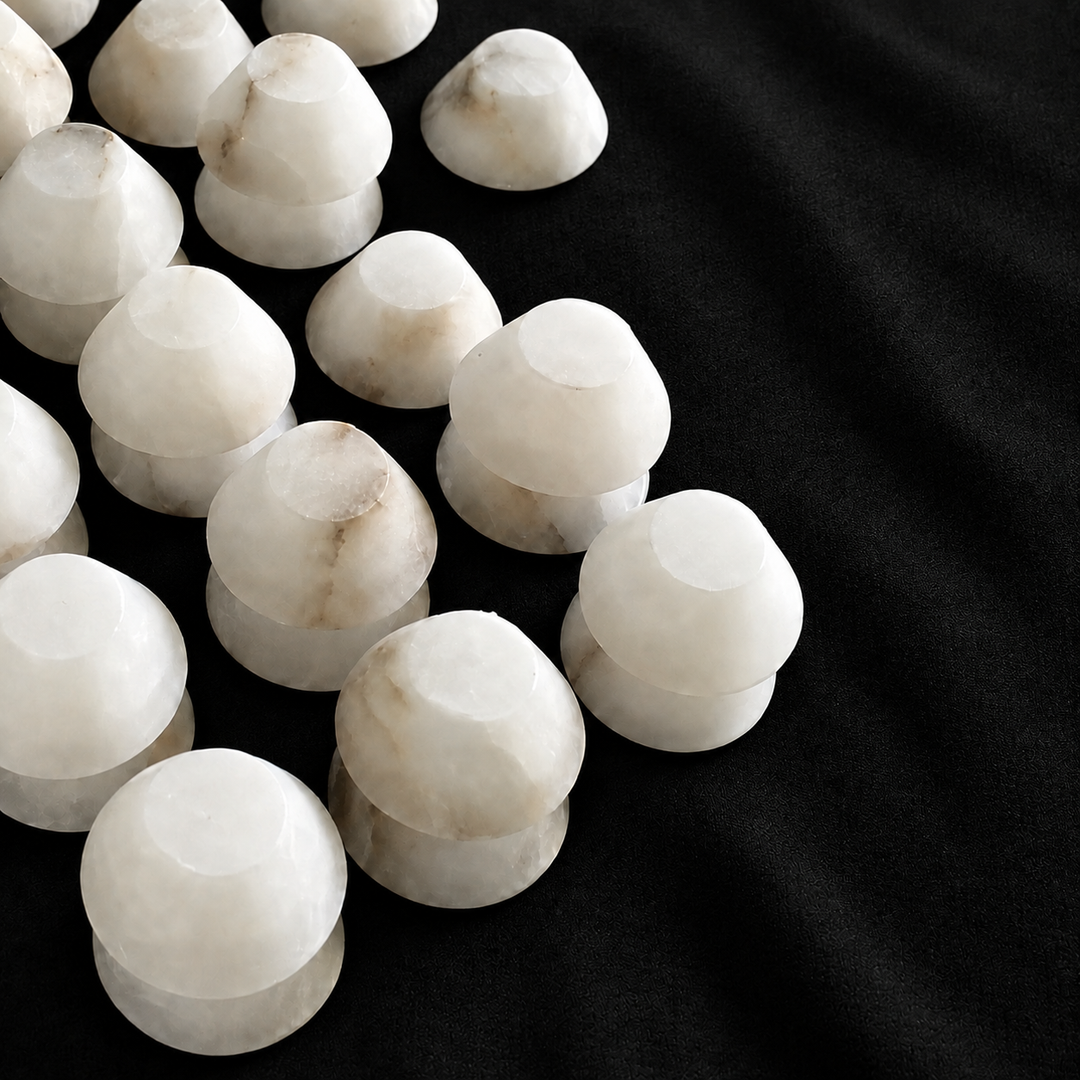 White marble chandelier shade components with subtle beige veining are arranged in rows on textured black fabric.