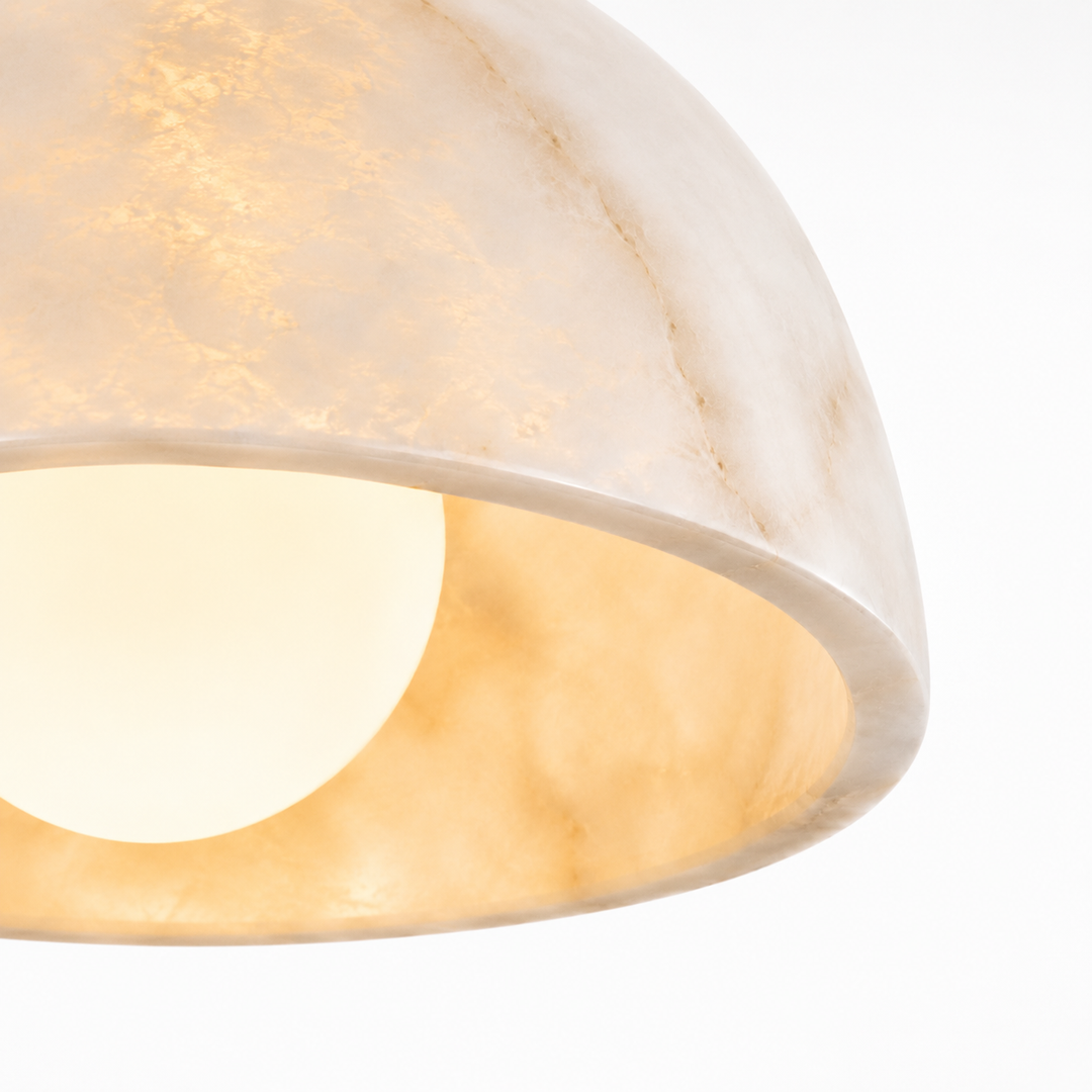 Close-up of a dome-shaped pendant light shade made of warm off-white stone or resin, glowing with a soft warm light against a white background.