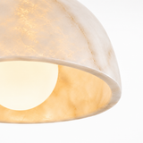 Close-up of a dome-shaped pendant light shade made of warm off-white stone or resin, glowing with a soft warm light against a white background.